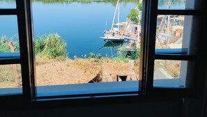 A view through a window with a curved frame, overlooking a calm lake with a docked boat and greenery in the background. - Eyaru Palace  (Luxor)