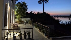 A terrace with potted plants, a palm tree, and a view of the water. - Eyaru Palace  (Luxor)