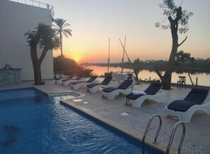 A swimming pool with lounge chairs and a sunset view. - Eyaru Palace (Luxor)