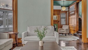 A living room with a beige sofa, a wooden coffee table, and a potted plant. There is a staircase with wooden railings and a chandelier. - Spacious 5-bedroom house with parking and everything you need in charming Elyria (Elyria)