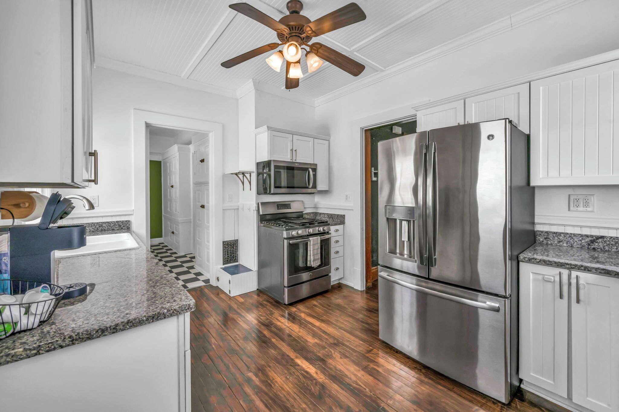 A modern kitchen with white cabinetry, stainless steel appliances, and a wooden floor.