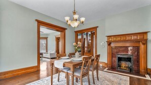 A dining room with a wooden table, chairs, and a chandelier. There is a fireplace with a brick surround and a rug on the floor. - Spacious 5-bedroom house with parking and everything you need in charming Elyria (Elyria)