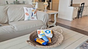 Una sala de estar con un sofá, una mesa de centro con una cesta tejida que contiene artículos de aseo, y una cocina al fondo.