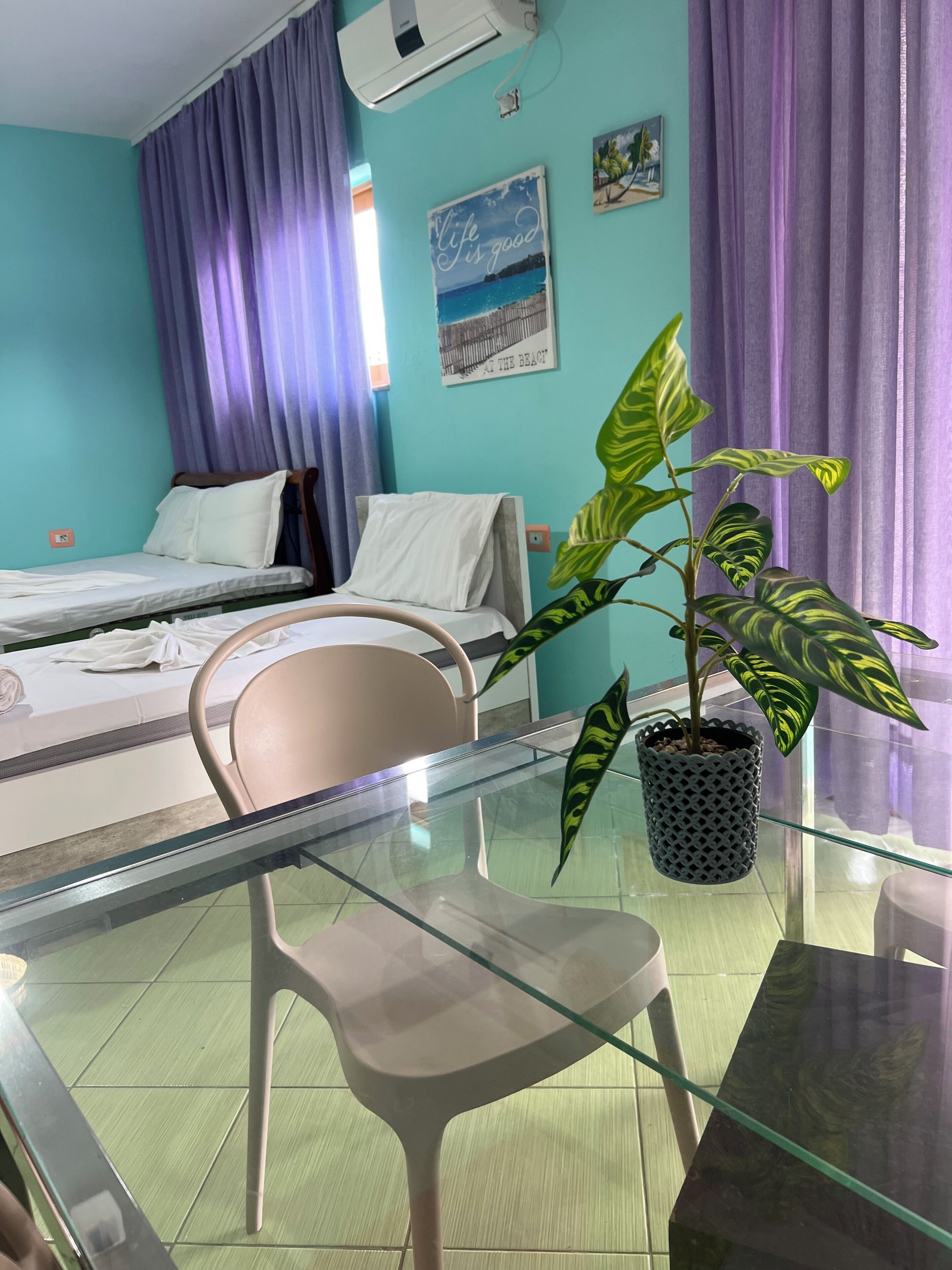 A hotel room with a bed, a chair, a table, and a potted plant.