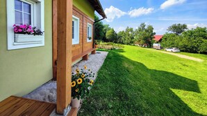A wooden house with a green exterior, a wooden deck, and a garden with flowers and grass. - ApaLuza - Ideal for families. Comfort & relaxation in nature. Horses and pool! (Stara Kamienica)