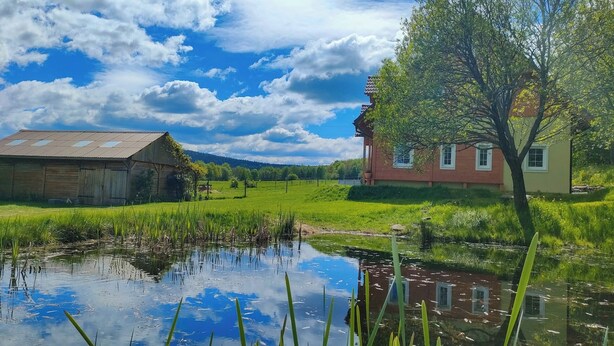A rural landscape with a wooden barn, a red house, and a pond. - ApaLuza - Ideal for families. Comfort & relaxation in nature. Horses and pool! (Stara Kamienica)