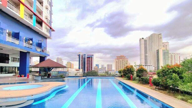 Una piscina con borde de baldosas, rodeada de vegetación y un paisaje urbano al fondo.