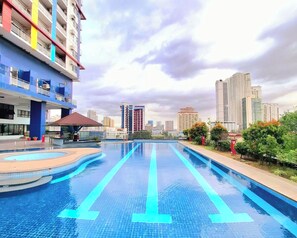 Une piscine dotée d’une terrasse carrelée, entourée de verdure et avec une vue sur la ville en arrière-plan.