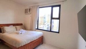 Un dormitorio con cama, ventana con cortinas, luz de techo y aire acondicionado de pared.