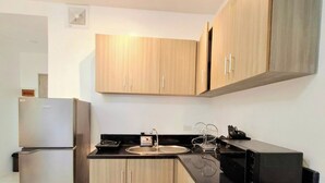 Una cocina moderna con armarios de madera, un refrigerador de acero inoxidable, una encimera negra y un microondas.