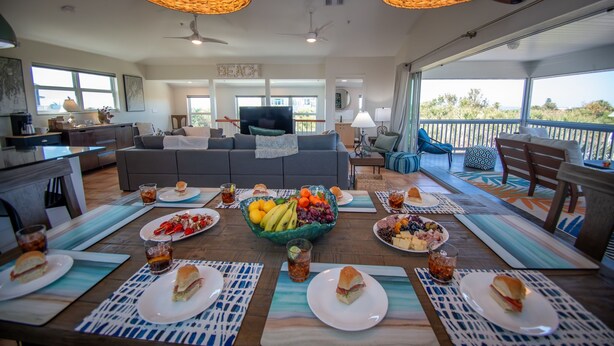 Amplia sala de estar con una gran mesa de comedor lista para una comida, un sofá y un televisor.