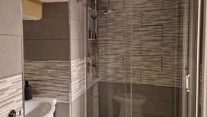 Et moderne badeværelse med en glasafskærmet brusekabine, et hvidt håndvaskarrangement og et flisebeklædt bagpanel.