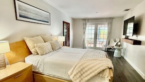 A modern bedroom with a wooden bed, a nightstand, a lamp, a TV, and a window with curtains. - YOUR PRIVATE RETREAT NEAR SIESTA KEY BEACH! (Sarasota)