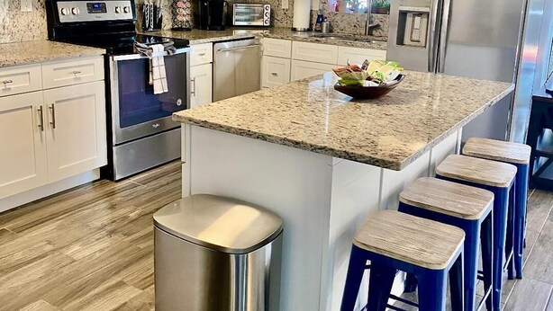 A modern kitchen with white cabinetry, stainless steel appliances, a granite countertop, and a central island with bar stools. - YOUR PRIVATE RETREAT NEAR SIESTA KEY BEACH! (Sarasota)