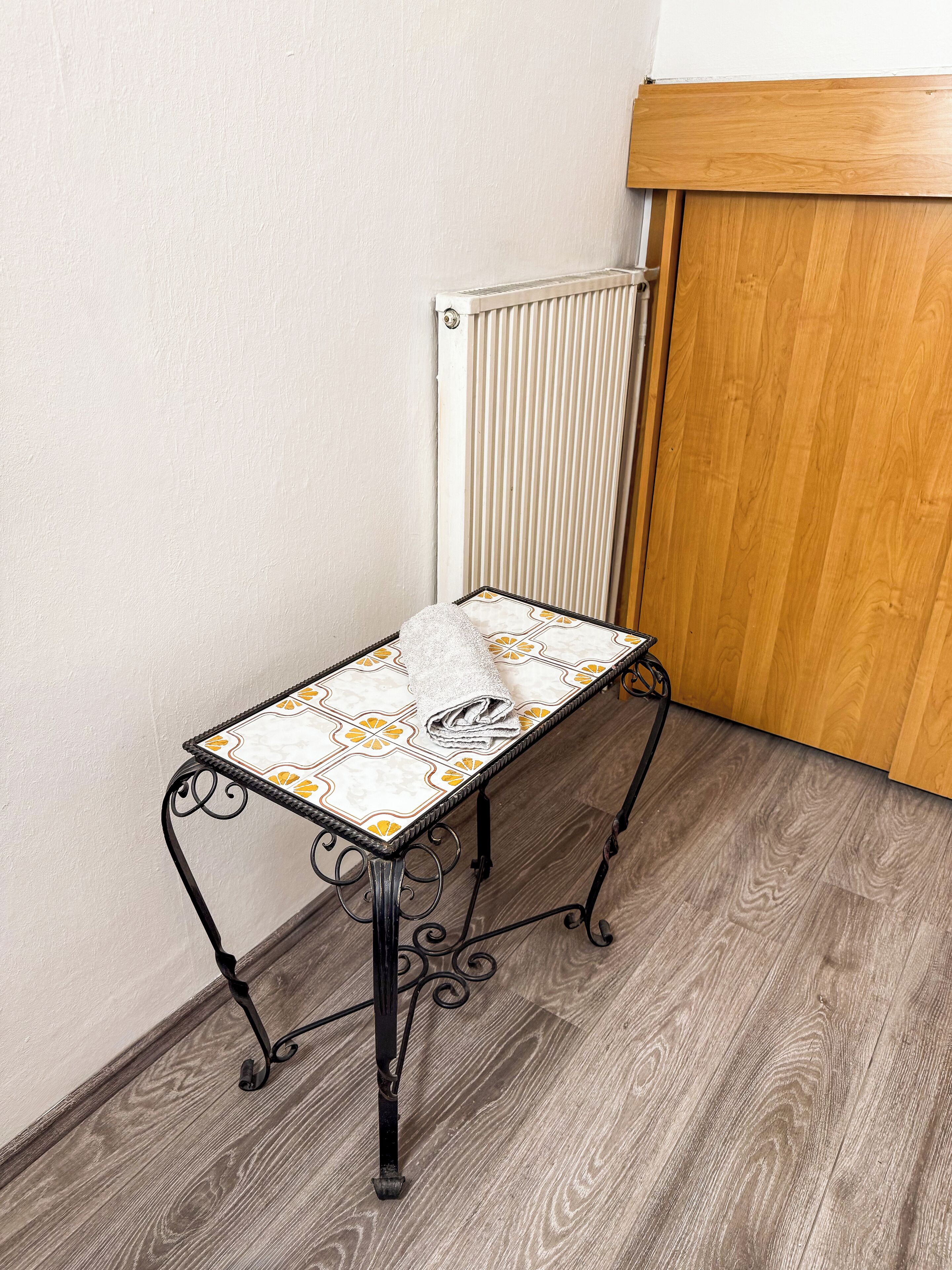 A small, ornate metal table with a patterned tablecloth, positioned near a radiator and wooden panel wall.