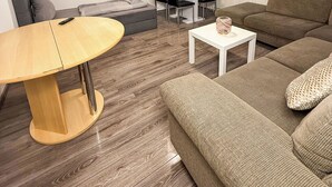 A modern living room with a round wooden table, a brown sofa, a white coffee table, and a TV mounted on the wall. - Ruhr Business Apartments Essen 7 beds Parking lot (Essen)