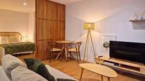 Un salon moderne comprenant un canapé, une petite table ronde, deux fauteuils, une lampe sur pied, un téléviseur posé sur un meuble en bois et un élément décoratif mural.
