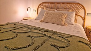 Un lit avec une tête de lit en osier, une lampe de chevet et un plaid à motifs.