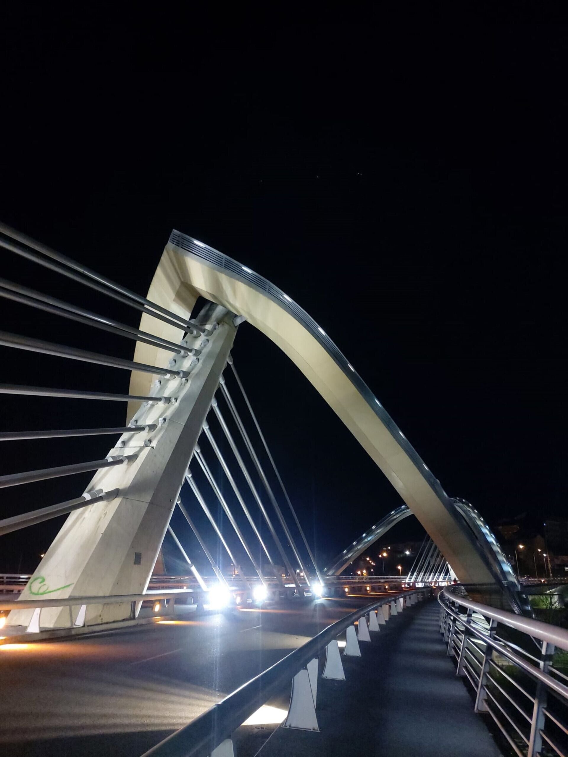 A nighttime view of a modern bridge with a curved arch and multiple cables.