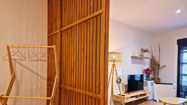 Une pièce avec un plancher en bois, un meuble pour la télévision avec un téléviseur à écran plat, une lampe et une plante.