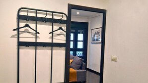 A bedroom with a bunk bed, a small table, and a chair. There is a door leading to another room with a couch and a framed picture on the wall.