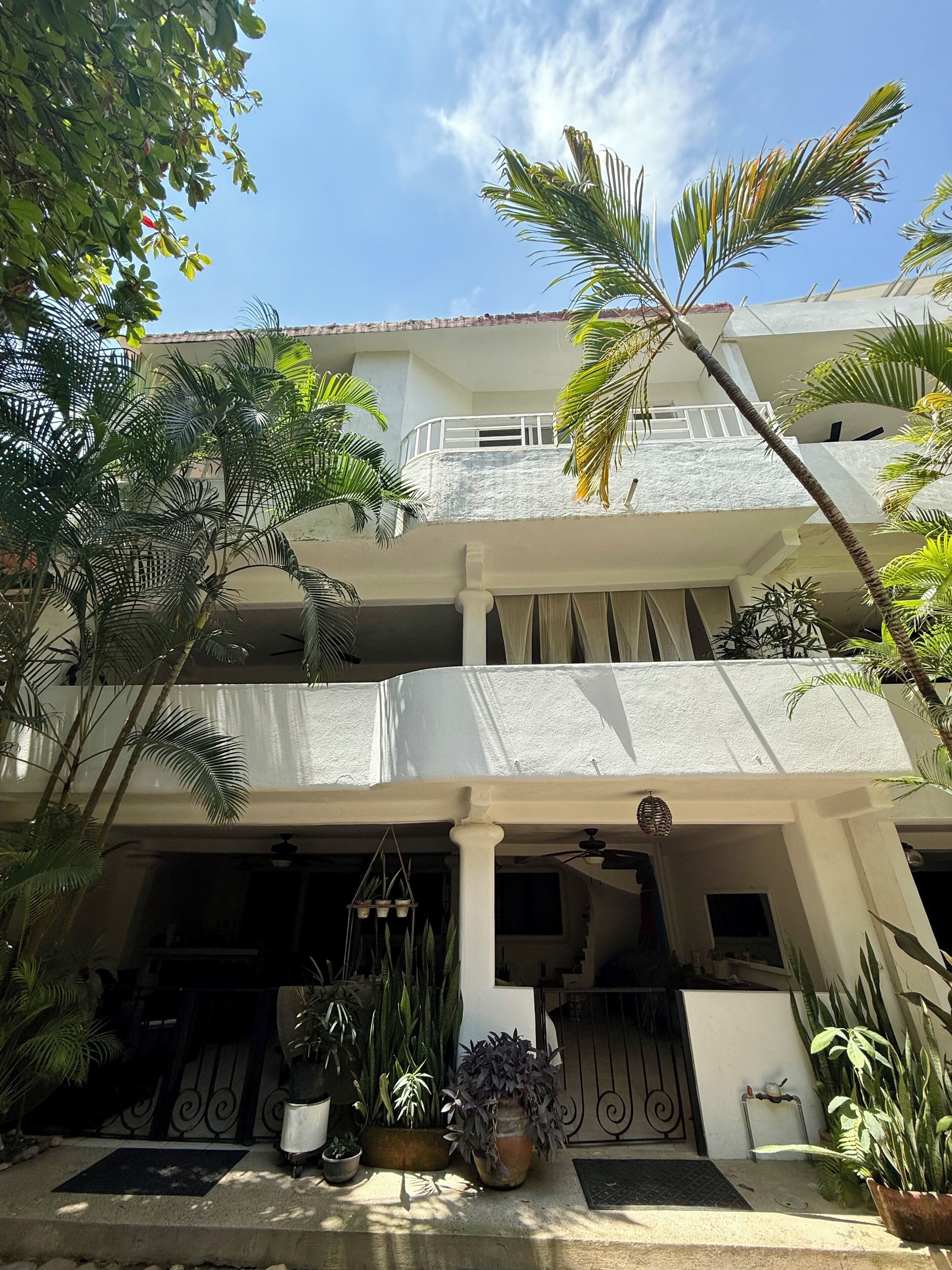 Un edificio de dos pisos con balcón, plantas en macetas y cielo despejado.