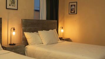 A hotel room with two beds, a nightstand with a lamp, an air conditioner, and framed pictures on the wall.