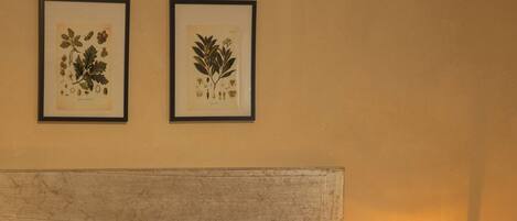 A neatly made bed with a brown bedspread and white pillows, a wooden headboard, and two framed botanical prints on the wall.