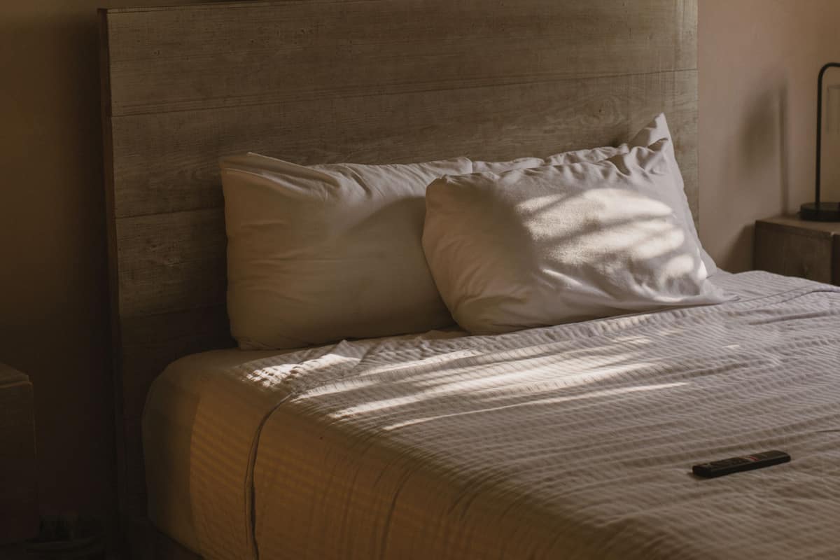 Uma cama bem arrumada com cabeceira, mesa de cabeceira e um quadro na parede.