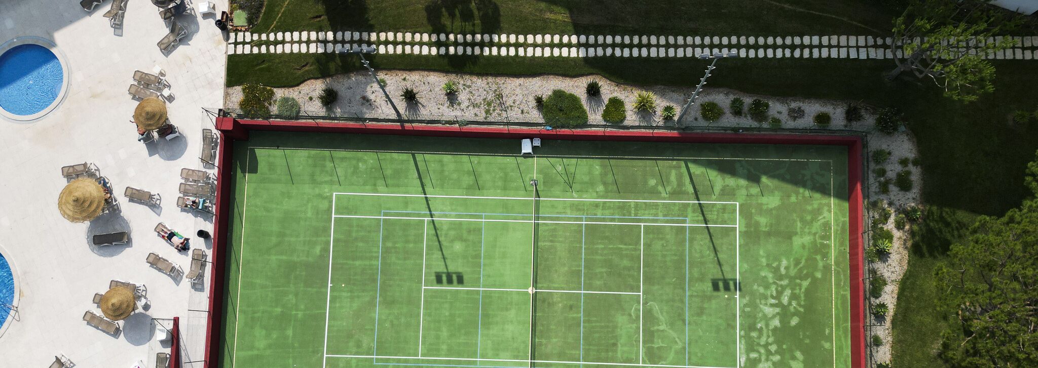 An aerial view of a tennis court with surrounding seating and a pool.