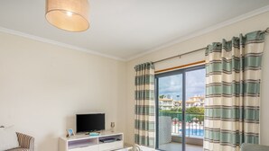 A living room with a TV, a sofa, a coffee table, and a balcony with striped curtains.