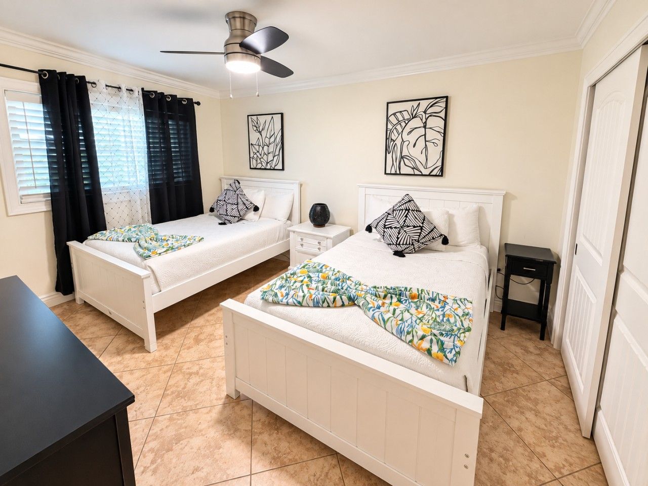 A bedroom with two beds, a ceiling fan, artwork on the walls, and a tiled floor.