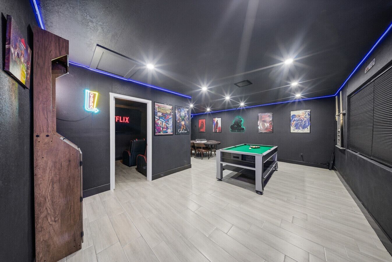 A room with a pool table, a door leading to a seating area, and a neon sign for Netflix.