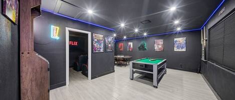 A room with a pool table, a door leading to a seating area, and a neon sign for Netflix.