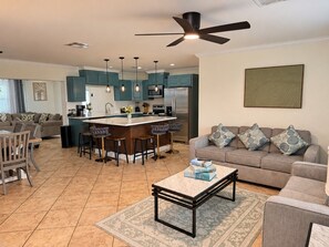 A modern kitchen with teal cabinets, a central island with stools, and a dining area with a table and chairs. - Luxury Getaway In Naples | Pool & Elegant Remodel (Naples)