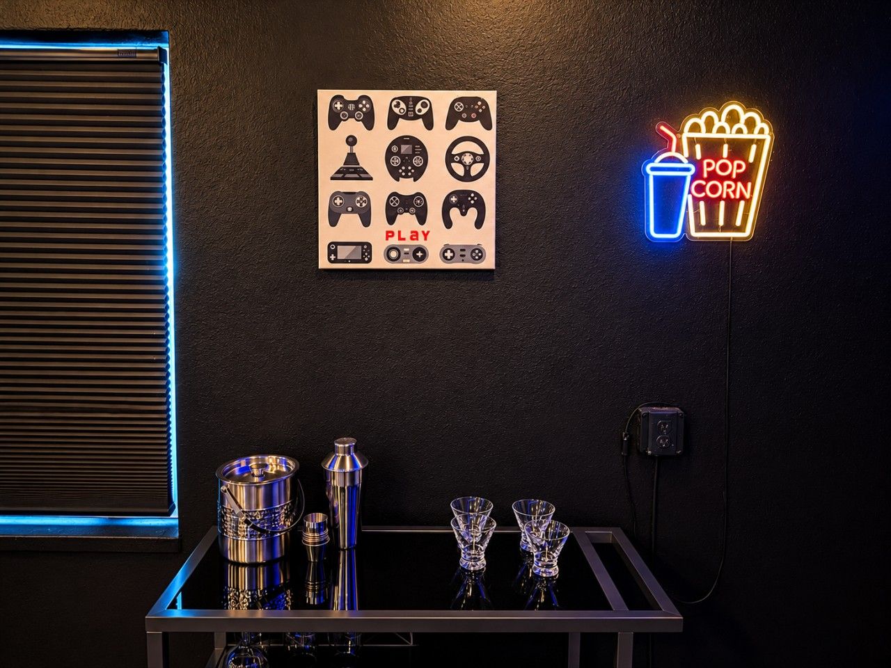 Et værelse med en neonskilte, en væg med ikoner af fjernbetjeninge og et barområde med glas og flasker.
