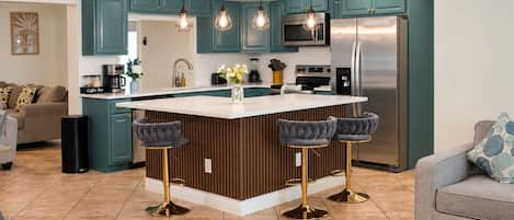 A modern kitchen with teal cabinets, a stainless steel refrigerator, and a central island with bar stools.