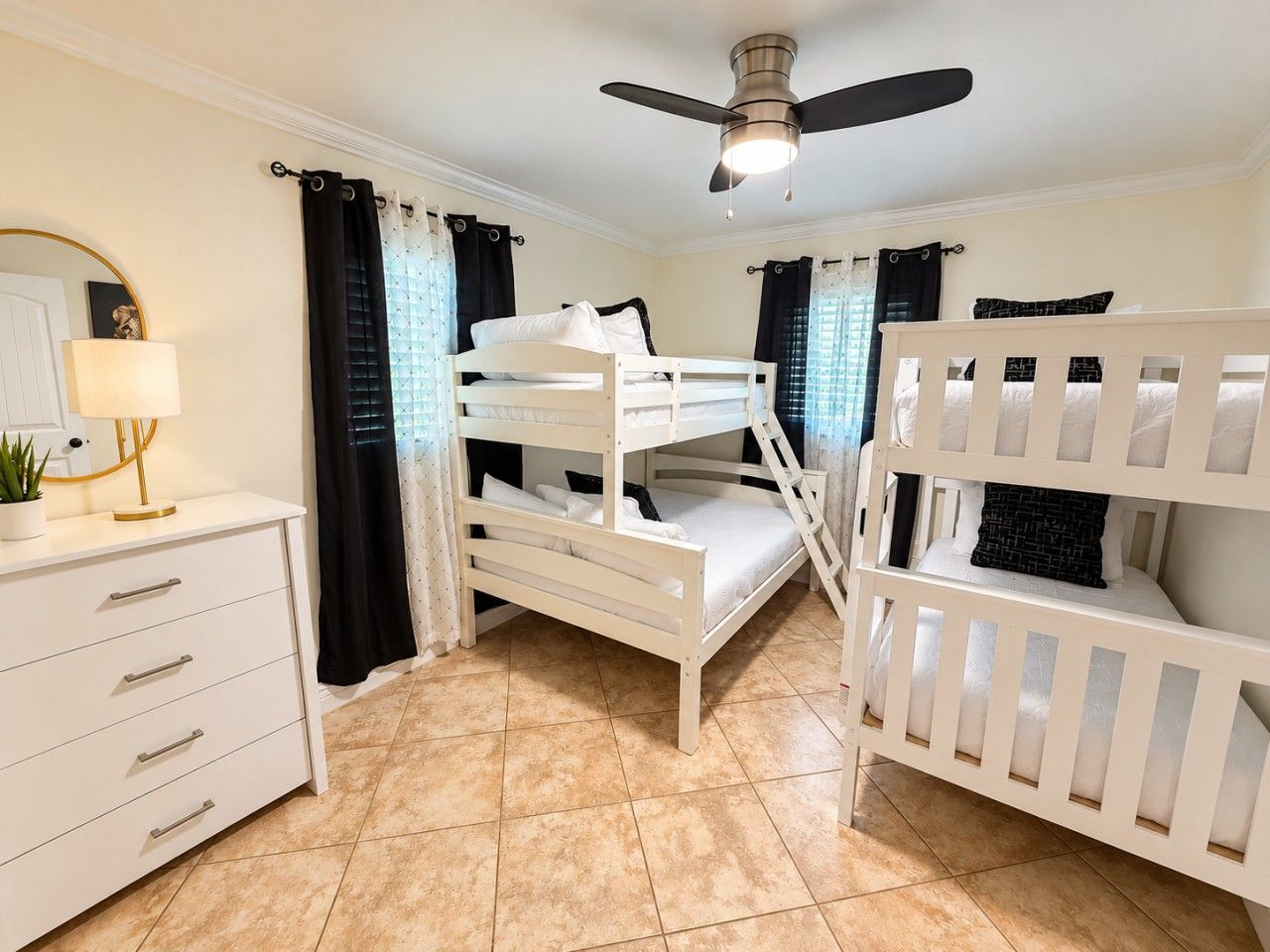 A room with bunk beds, a desk with drawers, a lamp, and a ceiling fan.