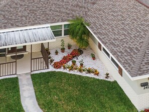 A two-story house with a covered porch, a small garden with various plants, and a visible number '247' on the side. - Luxury Getaway In Naples | Pool & Elegant Remodel (Naples)