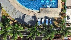 Eine Vogelperspektive auf ein Schwimmbecken mit einem zentralen, kreisförmigen Bereich, umgeben von einer gefliesten Liegefläche und einem überdachten Sitzbereich.
