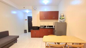 Ein kompakter Wohnbereich mit Sofa, Esstisch mit Stühlen, Küchenzeile mit Schränken, Kühlschrank und einer Uhr an der Wand.