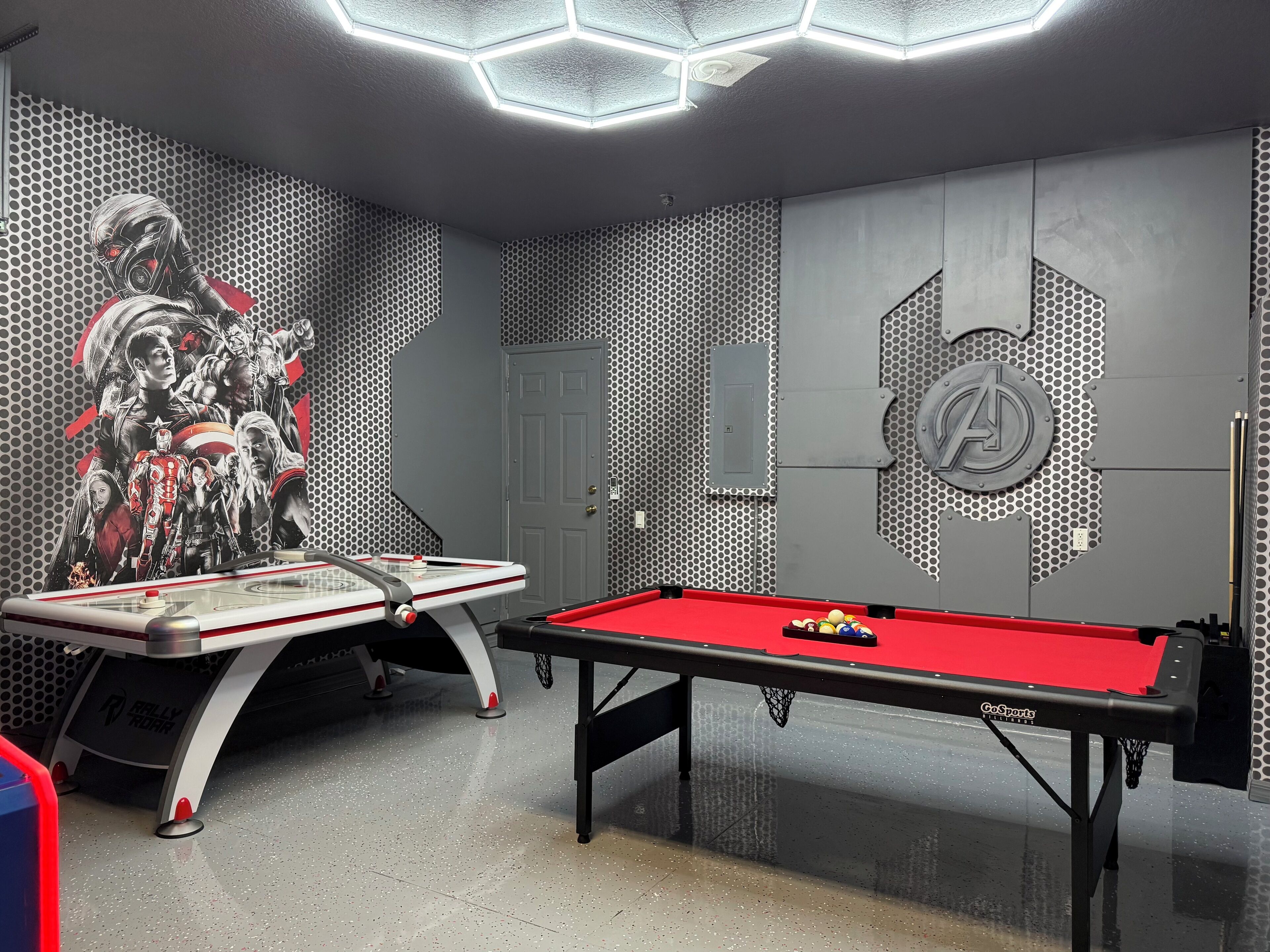 A pool table in a room with a hexagonal ceiling light fixture, a door, and a wall with a hexagonal pattern and a large logo.