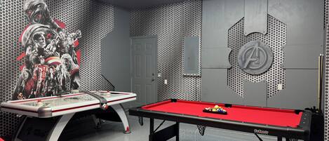 A pool table in a room with a hexagonal ceiling light fixture, a door, and a wall with a hexagonal pattern and a large logo.