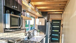 A modern kitchen with a central island, stainless steel appliances, wooden ceiling, and a view into the adjacent living area. - Modern Adirondack Getaway (Malone)