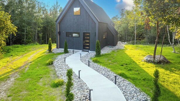 A modern barn-style building with a sloped roof, surrounded by a well-maintained lawn and trees. - Modern Adirondack Getaway (Malone)