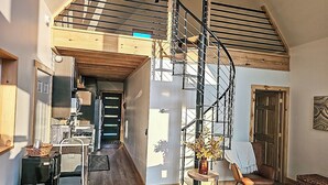 A spacious loft with a spiral staircase, wooden floors, and a dining area with modern furniture. - Modern Adirondack Getaway (Malone)