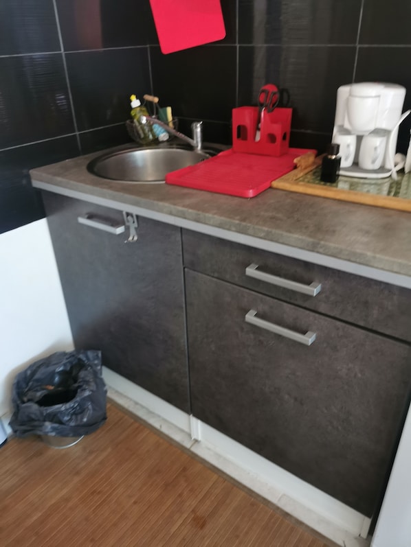A kitchen with a sink, a red cutting board, a coffee maker, and a trash bin.