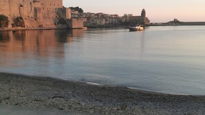 A waterfront view with a stone-paved area, a large building with towers, and a calm body of water. - Studio 16 mcarré kicnetteet frigo compartiment congelateur micro ondes (Perpignan,)