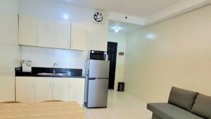 Una cocina moderna con armarios blancos, encimera negra y microondas integrado. En la zona de estar, hay una mesa de comedor con sillas y un sofá gris.