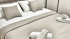 A neatly made bed with a grey headboard, white bedding, and a grey quilted blanket. - Lux Apartment Nina&Martina new 2025 (Split)